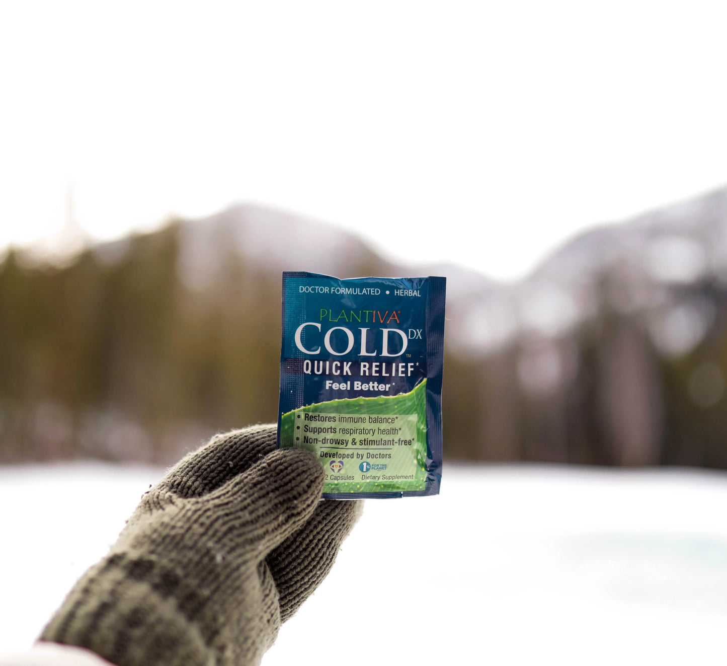A mittened hand holding a Cold Dx packet with a snowy outdoor background
