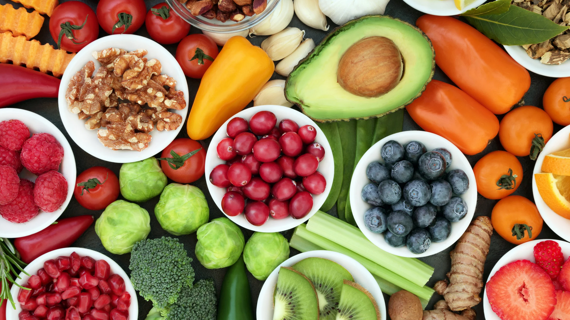 An array of healthy foods is displayed, including blueberries, tomatoes, walnuts, avocado, peppers, kiwi, pomegranate, turmeric, and more.