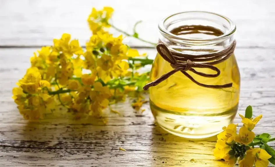 A flask of golden canola oil with canola flowers on a wooden surface