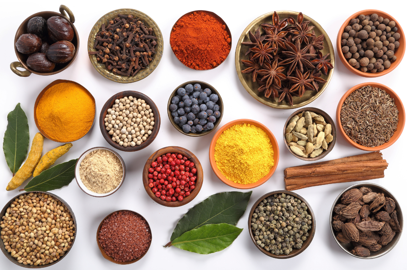 An array of herbs and spices is displayed, including cinnamon, allspice, cloves, cardamom, coriander, turmeric, bay leaf, juniper berry, cumin, and star anise.