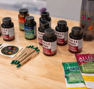 A variety of supplement bottles on a wooden table with Plantiva pens, stickers, and a water bottle