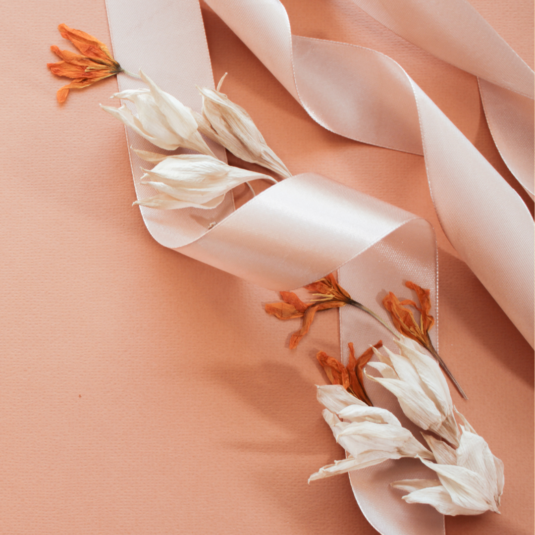A stem of flowers wrapped in a white ribbon against a peach surface