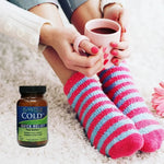 Person wearing colorful socks holding a mug with a bottle of Plantiva Cold Dx on a carpet.