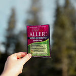 Hand holding a packet of AllerRx against a background of evergreen trees
