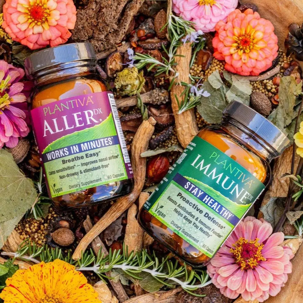 A bottle of AllerDx and a bottle of ImmuneDx in a wooden bowl with flowers and other botanicals