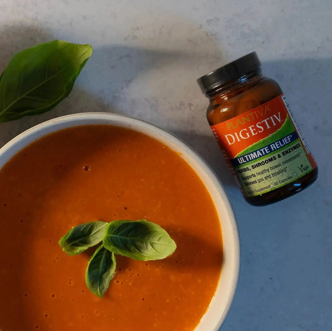 Bowl of tomato soup with basil leaves and a bottle of Digestiv on a counter