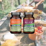 A bottle of AllerDx and a bottle of Digestiv on a background of a picnic table laden with food