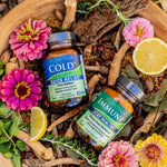 A bottle of ColdDx and a bottle of ImmuneDx in a wooden bowl with flowers and other botanicals