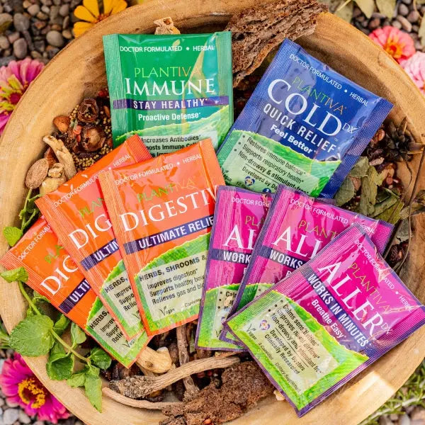 Packets of ImmuneDx, ColdDx, Digestiv and AllerDx in a wooden bowl with flowers and other botanicals