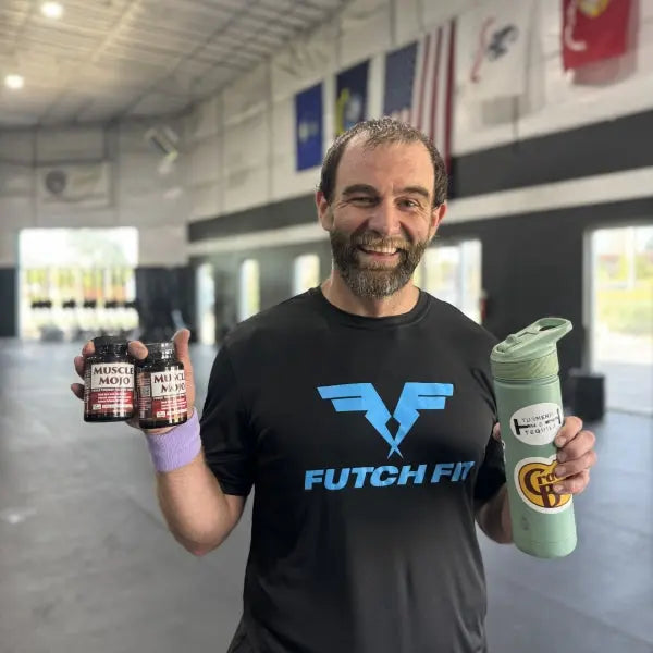 Man in black shirt at gym holding a water bottle and 2 bottles of Muscle Mojo