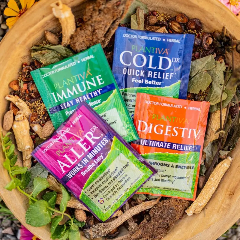 Packets of ImmuneDx, ColdDx, AllerDx and Digestiv in a wooden bowl with flowers, leaves and other botanicals