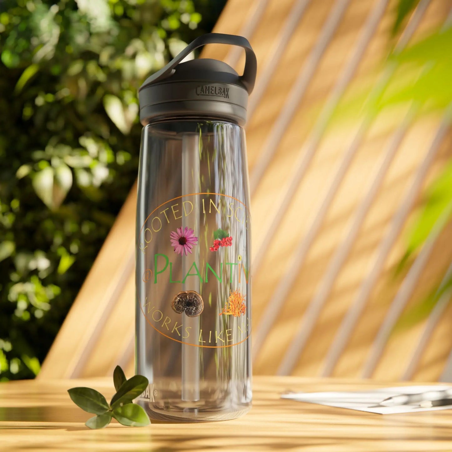 Clear water bottle with black lid and Plantiva logo, on a wooden surface with plants