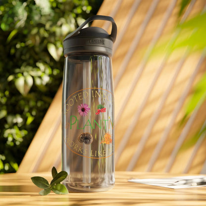 Clear water bottle with black lid and Plantiva logo, on a wooden surface with plants