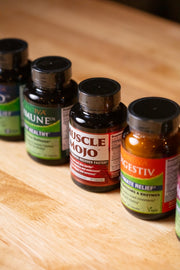 Four dark supplement bottles with black caps lined up on a light wood surface. Visible labels include ImmuneDx, Muscle Mojo, and Digestiv.
