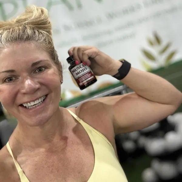 Woman in yellow workout clothes smiling and holding a bottle of Muscle Mojo
